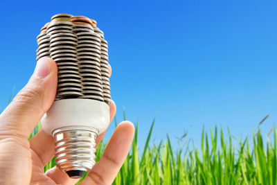 Cropped image of hand holding coins shaped as light bulb against clear blue sky