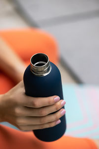 Close-up of female hand holding reusable steel thermo water bottle isolated on background color
