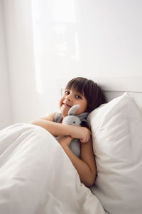 Child boy lies in a white children's bed with a blanket in a room with toys rabbits hug