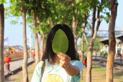Mature woman holding leaf in front of face while standing by trees