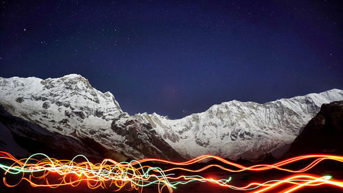 Light trails on snowcapped mountain against sky at night