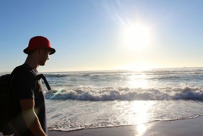 Young man standing at sea shore against bright sky