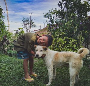 Portrait of boy embracing dog on field against plants