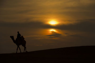 Silhouette man riding horse on landscape against sky during sunset