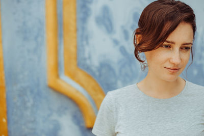 Portrait of a thoughtful young woman standing against a blue wall