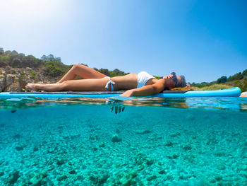 Woman lying on paddleboard in sea against sky