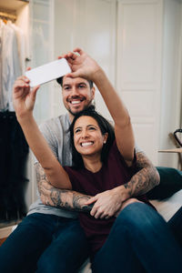 Smiling couple taking selfie on mobile phone while resting on bed in bedroom
