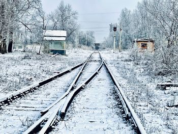 Snow covered railroad tracks by bare trees during winter