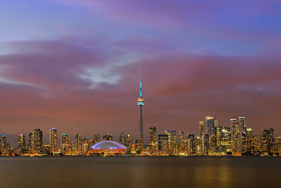 Illuminated buildings in city against cloudy sky