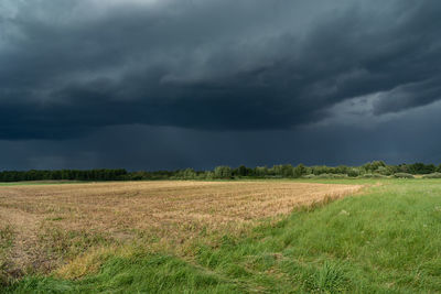 Dark storm clouds over the stubble and green meadow