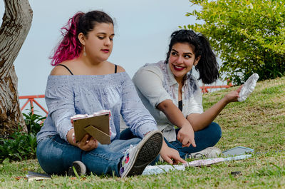 Full length of friends holding mirror frames while sitting at park