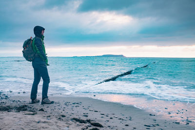 Hiker is looking out to sea stack. evening at calm blue sea, stony beach.