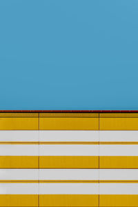 Low angle view of yellow wall against clear blue sky