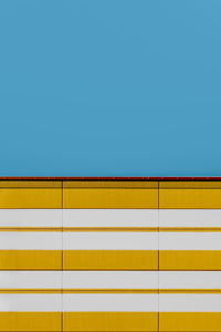 Low angle view of striped yellow wall against clear blue sky