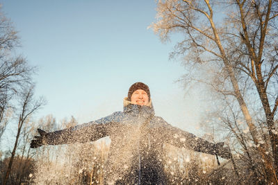 Low angle view of cheerful man with arms outstretched standing against clear sky