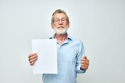 Portrait of senior man holding paper against white background