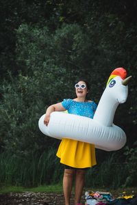 Woman holding toy while standing against trees