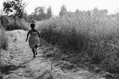 Rear view of woman running amidst grassy field on sunny day