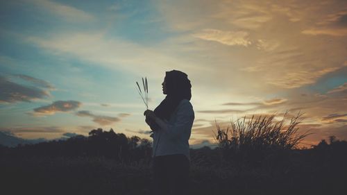 Low section of woman standing on field against sky during sunset