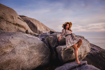 Man sitting on rock by sea against sky