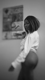 Side view of young woman standing against wall at home