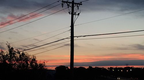 Silhouette electricity pylon against dramatic sky during sunset