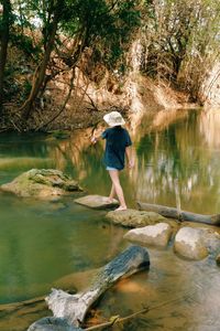 Full length of woman standing on rock by lake in forest