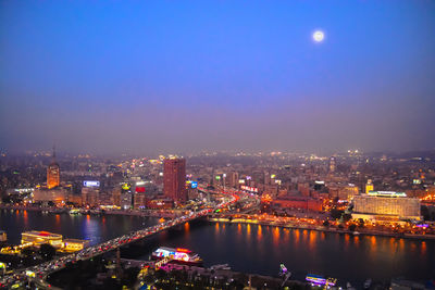 Illuminated city by river against sky at night