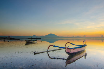 Boat moored on beach against sky during sunset