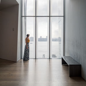 Woman looking through window while standing at home