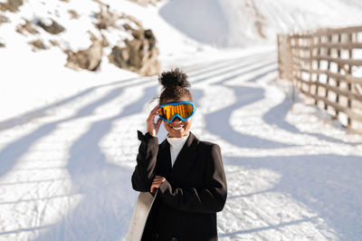 African american woman with goggles and a snowboard on a snowy mountain during winter