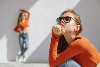 Twin sisters in sunglasses and identical clothes posing in contrast sunlight. focus on foreground.