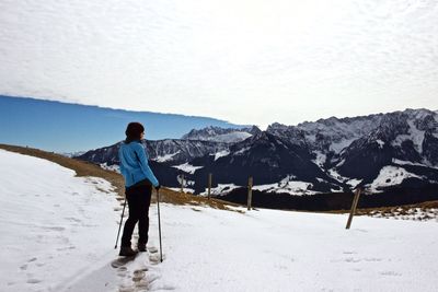 Rear view of woman holding ski poles while standing on snowcapped mountain