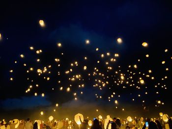 Group of people at illuminated street lights against sky at night