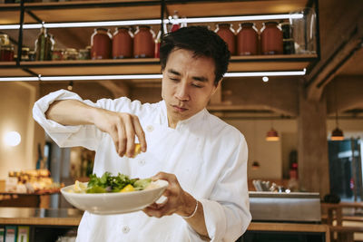 Close-up of male chef squeezing lemon juice on salad at commercial kitchen