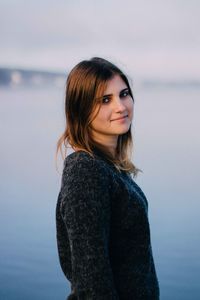 Portrait of young woman standing against lake