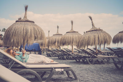 Full length of woman lying on lunge chair at beach against sky