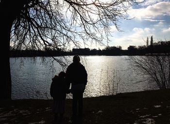 Silhouette bare trees by lake at sunset