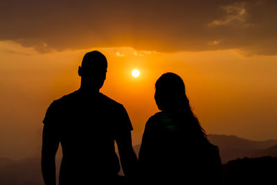 Silhouette couple standing against orange sky