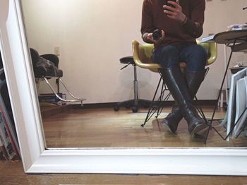 Low section of man with reflection on mirror holding camera lens at home