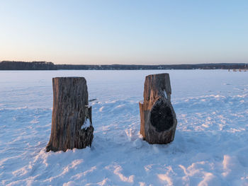 Wooden post in frozen lake during sunset