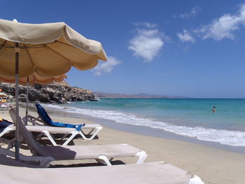 Empty lounge chairs at beach against sky