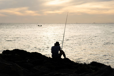 Silhouette of a fisherman with fishing rod sitting on the rocks of the rio vermelho beach 