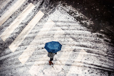 Person under blue umbrella crossing street in winter