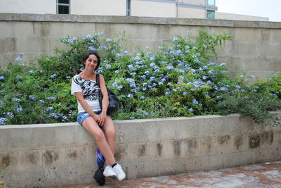 Portrait of woman sitting on retaining wall against plants