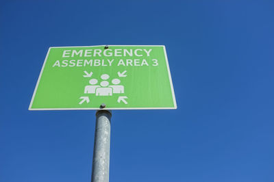 Low angle view of road sign against clear blue sky