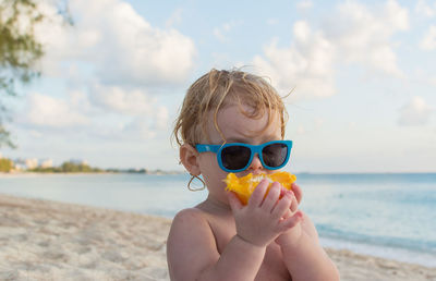 Portrait of shirtless boy holding sunglasses at beach