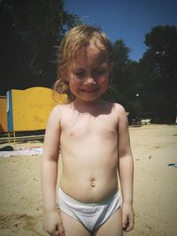 Topless little girl crying at beach on sunny day