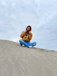 Young woman sitting on rock against sky