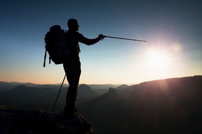 Sharp silhouette of a tall man on the top of the mountain with sun in the frame